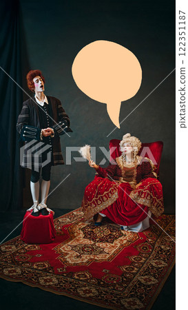 Young man, court servant in red wig standing next to elderly woman, medieval empress and singing to her against dark background with abstract speech bubble 122351187
