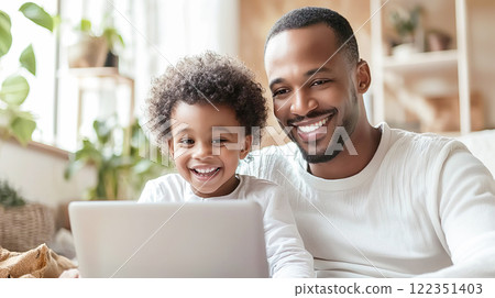 A black father and his child happily standing side by side looking at a laptop 122351403