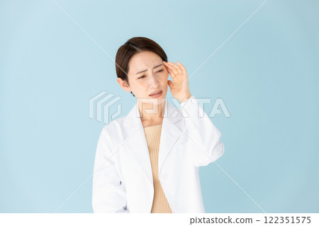 Woman in white coat with headache Woman in white coat with headache 122351575