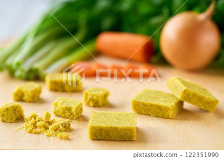 Bouillon cubes and fresh vegetables for soup on kitchen wooden table, selective focus. Bouillon cubes and fresh vegetables for soup on kitchen wooden table, selective focus. 122351990