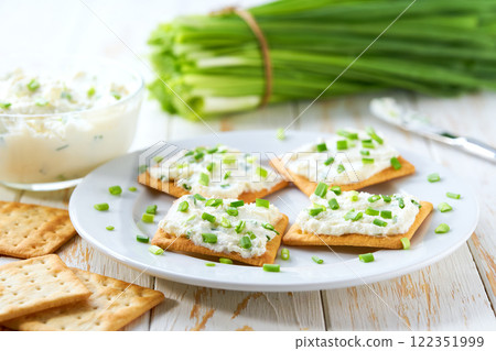 Crispy crackers and a glass bowl with a cream cheese spread and cut chives on a light kitchen table. Crispy crackers and a glass bowl with a cream cheese spread and cut chives on a light kitchen table. 122351999