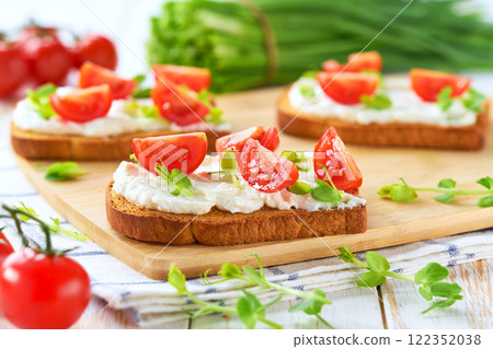 Sandwiches or toast with tomatoes cherry, cream cheese, olive oil and microgreen on a plate on white table. 122352038