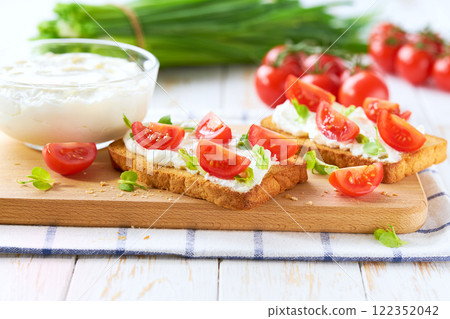 Sandwiches or toast with tomatoes cherry, cream cheese, olive oil and microgreen on a plate on white table. Sandwiches or toast with tomatoes cherry, cream cheese, olive oil and microgreen on a plate on white table. 122352042