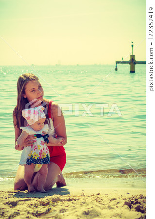 Woman hugging baby on beach near water Woman hugging baby on beach near water 122352419