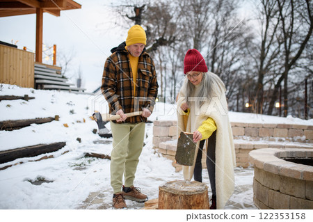 Older husband teaching his wife how to cut wood. He is preparing logs for the fireplace. 122353158