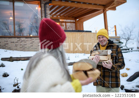 Older couple preparing logs for the fireplace in their cottage. Weekend in nature. Older couple preparing logs for the fireplace in their cottage. Weekend in nature. 122353165