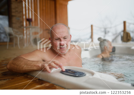 Older man setting up a hot tub, using control panel. Wellness getaway for senior couple. 122353256