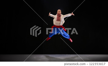 Performer leaps mid-air, arms wide open, with joyful expression and vibrant embroidered attire, capturing the essence of Hopak's celebratory spirit. 122353817