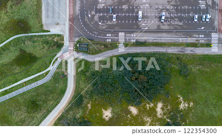 Aerial view of a parking lot with cars, crosswalks, paved roads, and green areas. Curved pathways and grasslands surround the parking space, blending urban and natural landscapes. Aerial view of a parking lot with cars, crosswalks, paved roads, and green areas. Curved pathways and grasslands surround the parking space, blending urban and natural landscapes. 122354300