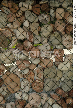 Large pebble stones secured by wire mesh fence for landscaping or erosion control Large pebble stones secured by wire mesh fence for landscaping or erosion control 122354756