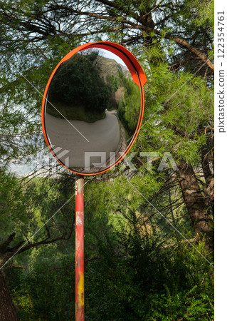 Convex Road traffic Mirror Reflecting Scenic Curve framed by Dense Pine Branches with a Distant Sea View Convex Road traffic Mirror Reflecting Scenic Curve framed by Dense Pine Branches with a Distant Sea View 122354761