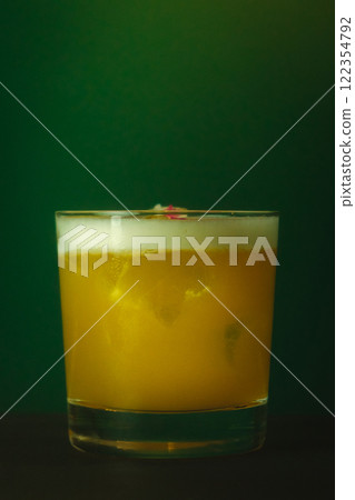 Vibrant Yellow Cocktail with Foam in Lowball Glass Refreshing Drink Against a Lush Green Backdrop Vibrant Yellow Cocktail with Foam in Lowball Glass Refreshing Drink Against a Lush Green Backdrop 122354792