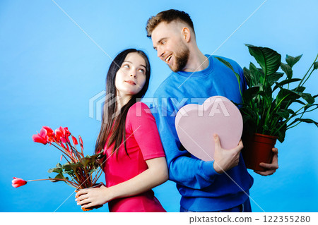 Loving boyfriend holding flowers pot and box and looking to girlfriend with present making romantic surprise 122355280