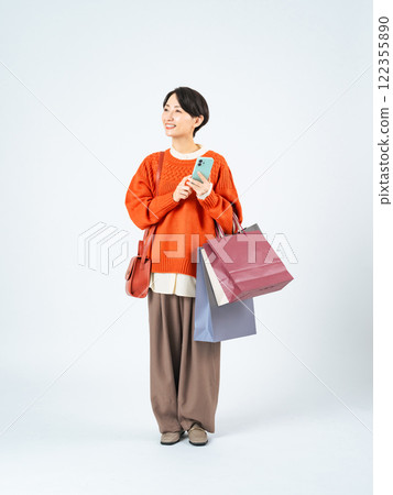 一名中年婦女拿著購物袋使用智慧型手機的全身照片 一名中年婦女拿著購物袋使用智慧型手機的全身照片 122355890