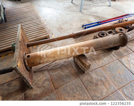 Large metal cylinder with a flange and scattered metal components in a workshop. Large metal cylinder with a flange and scattered metal components in a workshop. 122356235