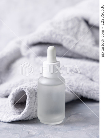 Clear glass dropper bottle with pipette near light grey bath towel closeup, cosmetic mockup Clear glass dropper bottle with pipette near light grey bath towel closeup, cosmetic mockup 122356536