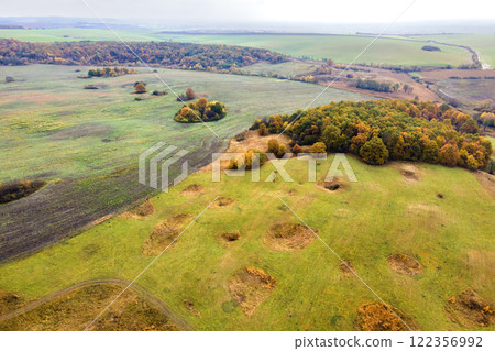 Aerial view of plowed agricultural fields with cultivated fertile soil prepared for planting crops between green woods in fall season Aerial view of plowed agricultural fields with cultivated fertile soil prepared for planting crops between green woods in fall season 122356992