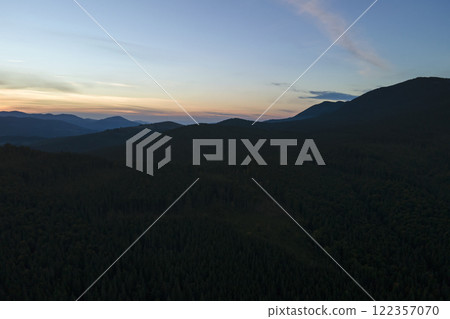Aerial view of green pine forest with dark spruce trees covering mountain hills at sunset. Nothern woodland scenery from above 122357070