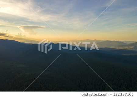Aerial view of dark mountain hills with bright sunrays of setting sun at sunset. Hazy peaks and misty valleys in evening Aerial view of dark mountain hills with bright sunrays of setting sun at sunset. Hazy peaks and misty valleys in evening 122357165