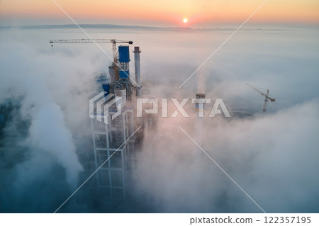 Aerial view of cement factory with high concrete plant structure and tower crane at industrial manufacturing site on foggy evening. Production and global industry concept. Aerial view of cement factory with high concrete plant structure and tower crane at industrial manufacturing site on foggy evening. Production and global industry concept. 122357195
