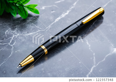 A black and gold pen sitting on top of a marble surface 122357348