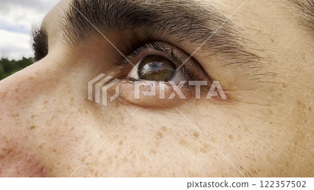 Focus on left brown eye of handsome sorrowful man looking into the distance. Portrait of unhappy male face with freckles outdoor. Upset facial expression of young guy. Close up Focus on left brown eye of handsome sorrowful man looking into the distance. Portrait of unhappy male face with freckles outdoor. Upset facial expression of young guy. Close up 122357502