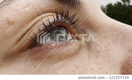 Focus on right green eye of attractive girl blinking and looking up. Portrait of a female pretty face. Calm facial expression of young woman. Tranquil sight of beautiful lady. 122357530