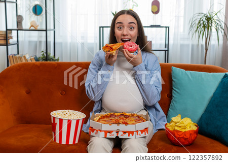 Pregnant woman eating unhealthy junk fatty fast food pizza popcorn crisp watching movie at home 122357892