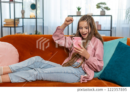 Happy girl child kid using mobile smartphone celebrate online game win good positive news at home 122357895