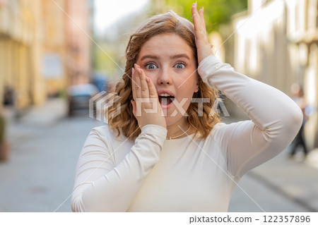Redhead woman looking surprised at camera shocked by sudden win good victory news wow in city street 122357896