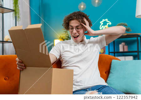 Happy customer man unpacking delivery parcel opening cardboard box receiving purchase gift at home 122357942