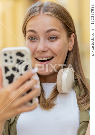 Excited happy joyful winner young woman using smartphone looking at screen standing on city street Excited happy joyful winner young woman using smartphone looking at screen standing on city street 122357958