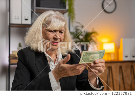 Elderly businesswoman in suit counting cash banknotes insufficient amount of money at home office Elderly businesswoman in suit counting cash banknotes insufficient amount of money at home office 122357981