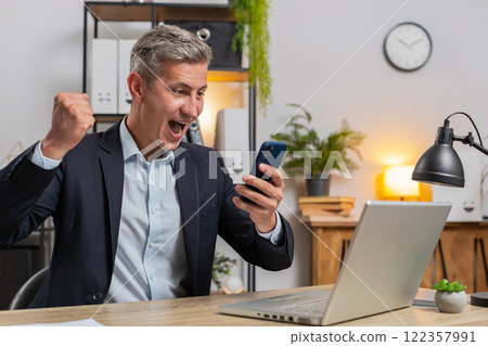 Happy Caucasian businessman celebrating success reading great news on smartphone at home office desk Happy Caucasian businessman celebrating success reading great news on smartphone at home office desk 122357991