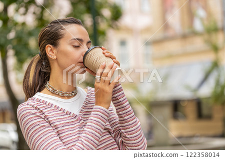 Happy smiling woman walking on city street enjoying morning coffee hot drink relaxing taking a break Happy smiling woman walking on city street enjoying morning coffee hot drink relaxing taking a break 122358014