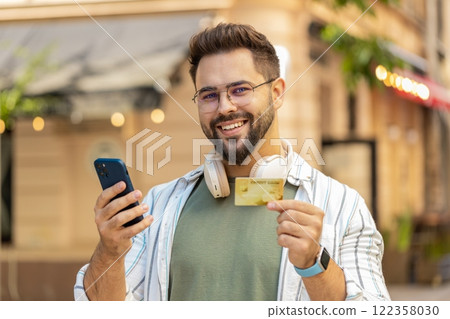 Man using credit bank card smartphone while transferring money, purchases online shopping outdoors Man using credit bank card smartphone while transferring money, purchases online shopping outdoors 122358030