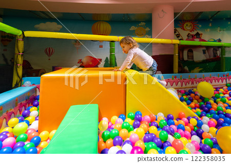 A playful child climbing a soft slide in a colorful ball pit at a vibrant indoor playground. A playful child climbing a soft slide in a colorful ball pit at a vibrant indoor playground. 122358035