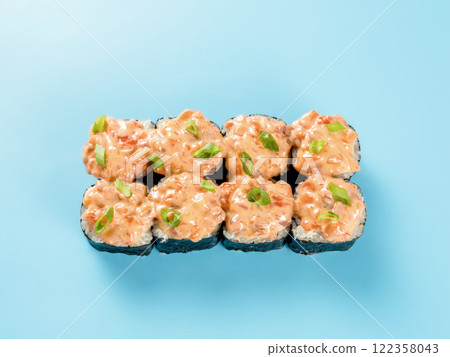 Top view of spicy salmon roll. Studio photography of Maki roll with spicy salmon, decorated green onion. Isolated on solid light blue background. Flat lay 122358043