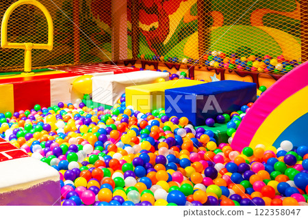 Colorful indoor ball pit with soft obstacles and a rainbow slide for kids. 122358047