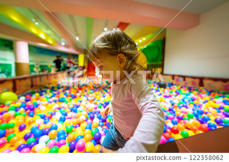 A curious child observing a colorful ball pit in a lively indoor playground. 122358062