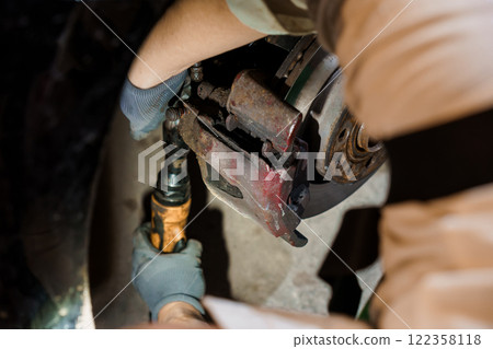 Skilled Mechanic Performing Brake Caliper Replacement in a Dimly Lit Garage Skilled Mechanic Performing Brake Caliper Replacement in a Dimly Lit Garage 122358118
