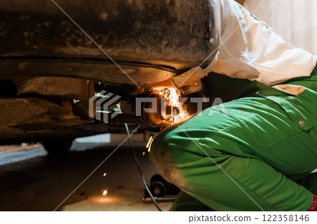 Mechanic Performing Brake Repair Under Car with Sparks Flying 122358146