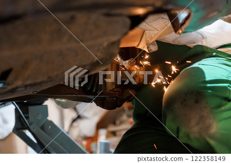 An Automotive Mechanic Working Underneath a Car with Sparks Flying 122358149