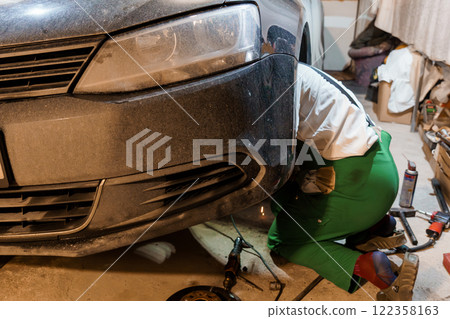 Car Mechanic Working Underneath a Vehicle in a Garage 122358163