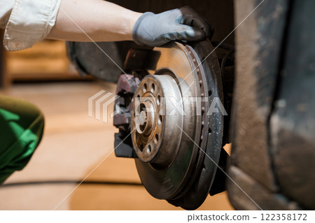 Close-up of a Mechanic Replacing a Car Brake Disc with Gloves on a Workshop Floor Close-up of a Mechanic Replacing a Car Brake Disc with Gloves on a Workshop Floor 122358172