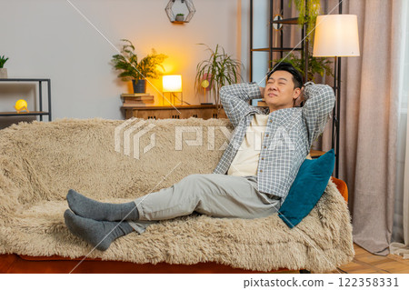 Happy carefree middle-aged Chinese man sitting comfortably on sofa thinking in living room at home Happy carefree middle-aged Chinese man sitting comfortably on sofa thinking in living room at home 122358331