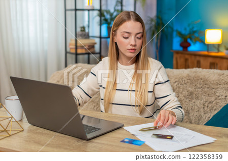 Caucasian woman checking bank account on laptop at home on table with credit cards, documents, happy 122358359