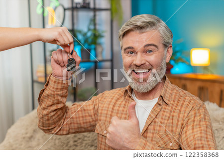 Mature man on sofa receiving keys to new apartment from realtor, smiling after lottery win at home 122358368