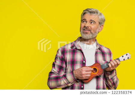 Happy mature man playing on toy guitar ukulele shaking head and dancing enjoying rhythm of music 122358374