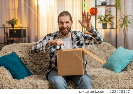 Young man receives delivery at home, sofa unboxing, quick happiness, big reveal, looking at camera Young man receives delivery at home, sofa unboxing, quick happiness, big reveal, looking at camera 122358397